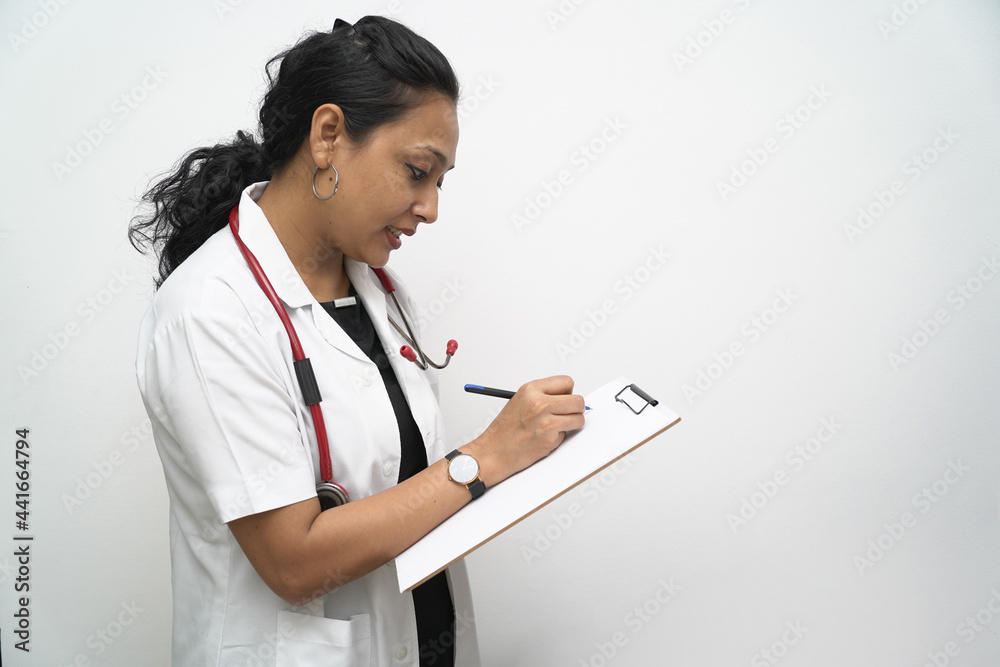 A south Indian female doctor in 30s writing medical prescription advice on a board with pen with white coat and red stethoscope in white background A south Indian female doctor in 30s writing medical prescription advice on a board with pen with white coat and red stethoscope in white background