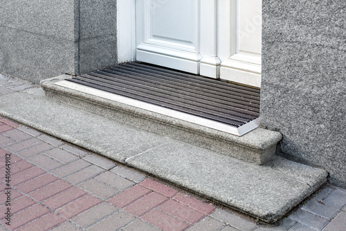 stone threshold with foot mat at the entrance door made of white wood and gray stone facade cladding of retro European architecture building closeup side view; nobody. photo