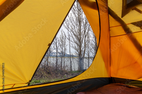 Looking outside of a yellow tent while camping in northern Canada with dry, spring time trees waiting to bloom for the summer on cloudy afternoon. Raining camp. 