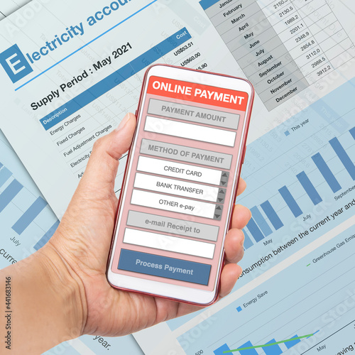 Hand holding smartphone showing electronic payment application with electricity bill on background.