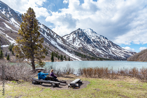 Woman and man couple sitting beside a lake in northern Canada with calm lake, blue sky and snow capped mountains. Scenic, iconic Canadian travel, tourism view.  photo