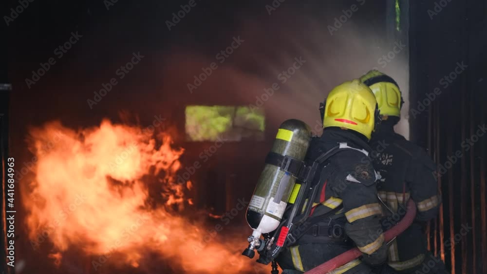 Two fireman or fire fighters try to extinguish flame of fire in room by using sprinkler to spray water to the base and around area but giant fire still cover all around.