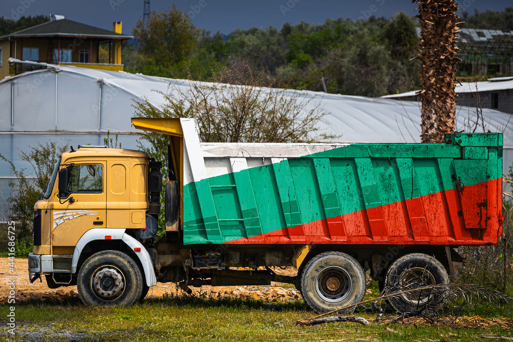 Obraz premium Dump truck with the image of the national flag of Bulgaria is parked against the background of the countryside. The concept of export-import, transportation, national delivery of goods