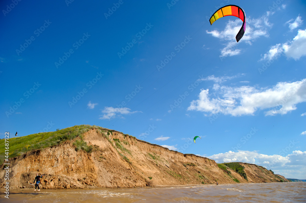 A kitesurfer walks along the shore and carries a kite in calm weather on a sunny summer day. A kitesurfer walks along the shore and carries a kite in calm weather on a sunny summer day.