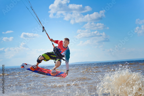 Kiteboarder surfing waves with kiteboard on a sunny summer day. A man performs a trick-jump on a surfboard.