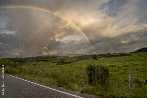 landscape of a rainbow on the road with some clouds and grass