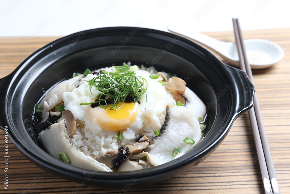 chef cook Hong Kong congee porridge with mixed seafood unagi, fish, prawn, squid, mushroom, egg and vegetables in black hot clay pot , chopstick spoon asian healthy halal menu chef cook Hong Kong congee porridge with mixed seafood unagi, fish, prawn, squid, mushroom, egg and vegetables in black hot clay pot , chopstick spoon asian healthy halal menu