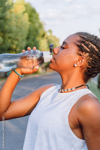 african-american girl drinking water after exercising on a sunny day