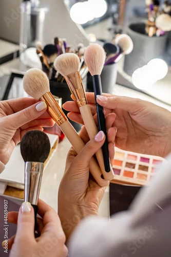 Obraz Close up hands of female makeup artist studying client choosing brush for cosmetics applying