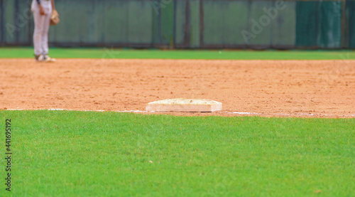 Joven jugador de béisbol en el campo en el fondo, caja de base en el centro, campo de béisbol verde y bien cuidado