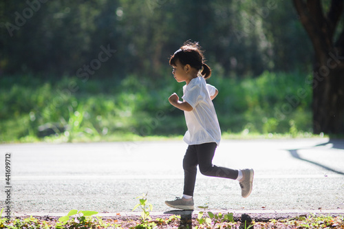 happy child girl running in the park in summer in nature. warm sunlight flare. asian little is running in a park. outdoor sports and fitness, exercise and competition learning for kid development.