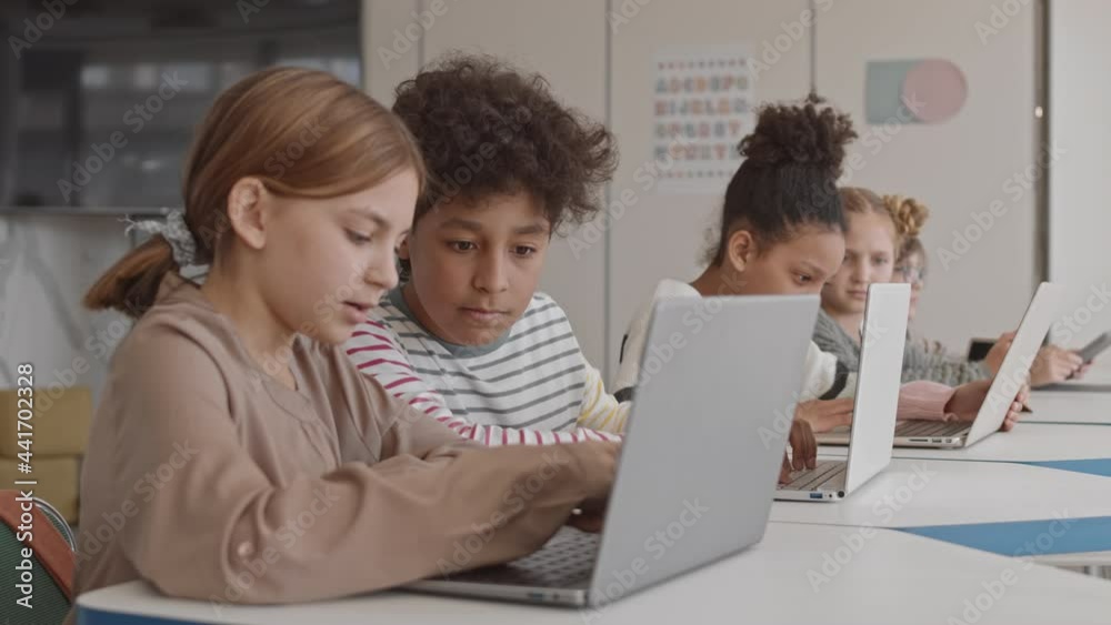 Medium shot of small group of smart multiethnic schoolchildren studying on laptops in modern IT class Medium shot of small group of smart multiethnic schoolchildren studying on laptops in modern IT class