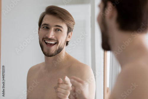 Happy excited guy having fun at mirror during daily bath procedures, talking to reflection, pointing finger, singing, dancing. Confident man feeling after-shower high, enjoying beauty care routine