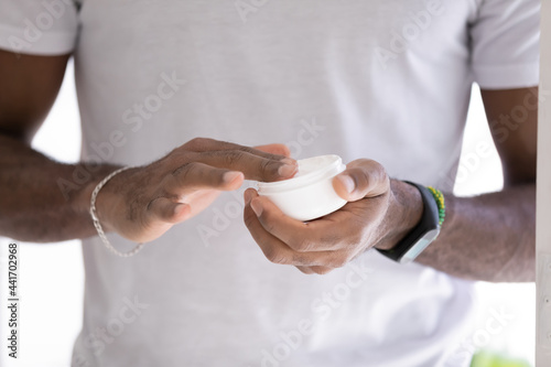 Obraz na płótnie Hands of mixed raced Black man in white t-shirt, taking moisturizing collagen cream, lotion, mask, hydrating balm from jar