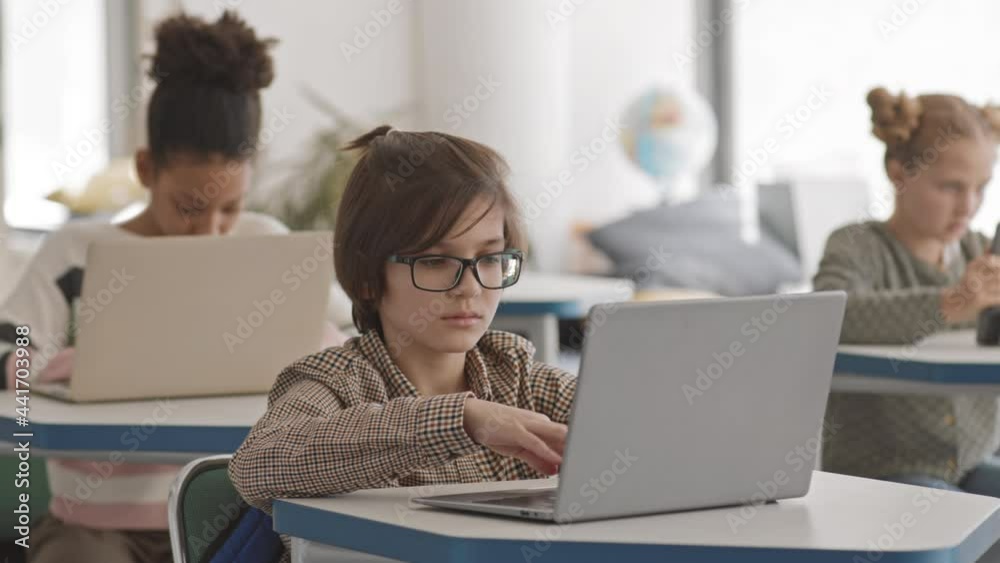 PAN medium slowmo of multiethnic schoolchildren of 5 or 6 grade sitting on by one at desks and studying on laptops or digital tablet in modern multicultural school PAN medium slowmo of multiethnic schoolchildren of 5 or 6 grade sitting on by one at desks and studying on laptops or digital tablet in modern multicultural school