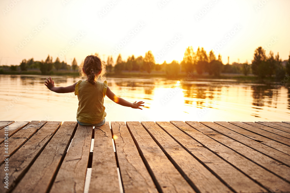 Φωτογραφία Silhouette of a child sitting on the wooden pier and enjoying heat summer evenin