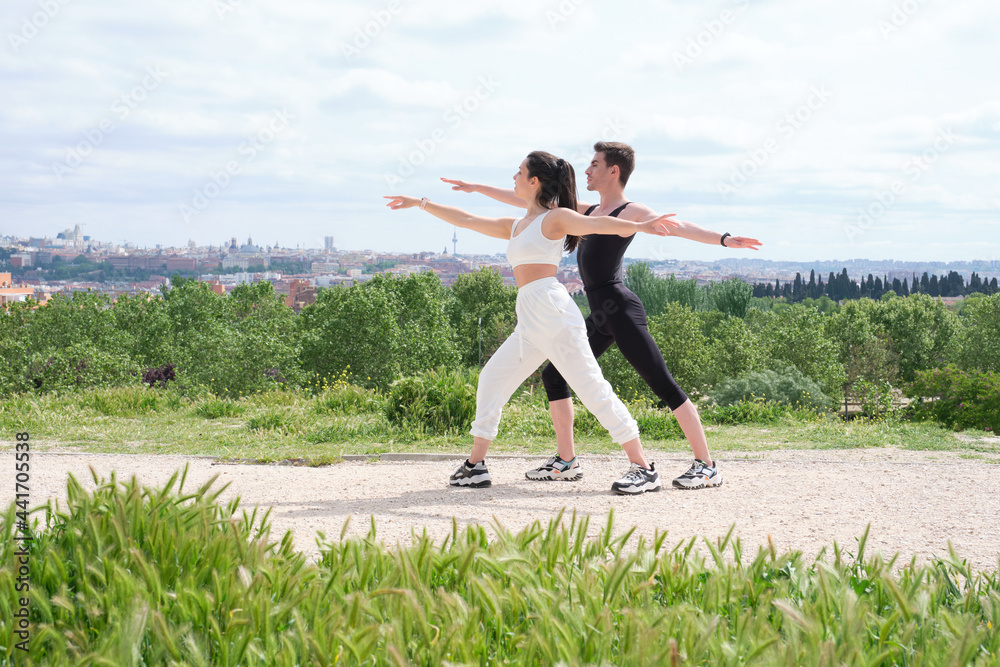 Young couple doing warrior two yoga pose in a park Young couple doing warrior two yoga pose in a park
