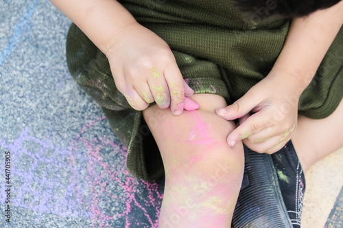 Kid playing with chalk color painting all over the floor and body.