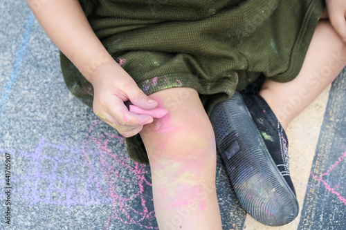 Kid playing with chalk color painting all over the floor and body.