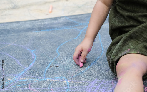 Kid playing with chalk color painting all over the floor and body.