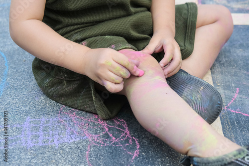 Kid playing with chalk color painting all over the floor and body.
