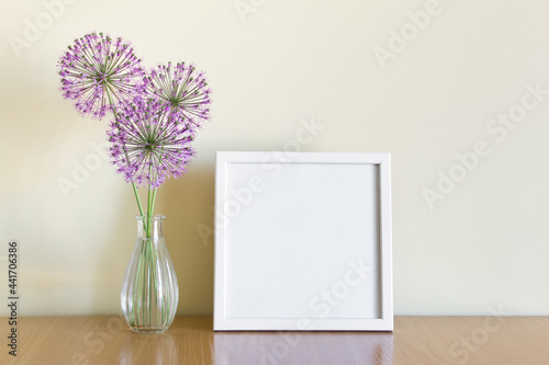 Mockup template of square white frame standing on wooden shelf with summer purple flowers.