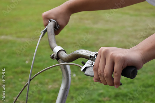 A young guy holds a handlebar of vintage bike which parked on the meadow background, soft and selective focus on hand.