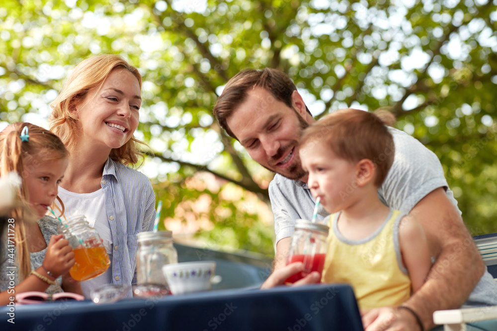 cheerful family sitting outdoor, drinking juices, enjoying. father helping his son to drink juice on straw.