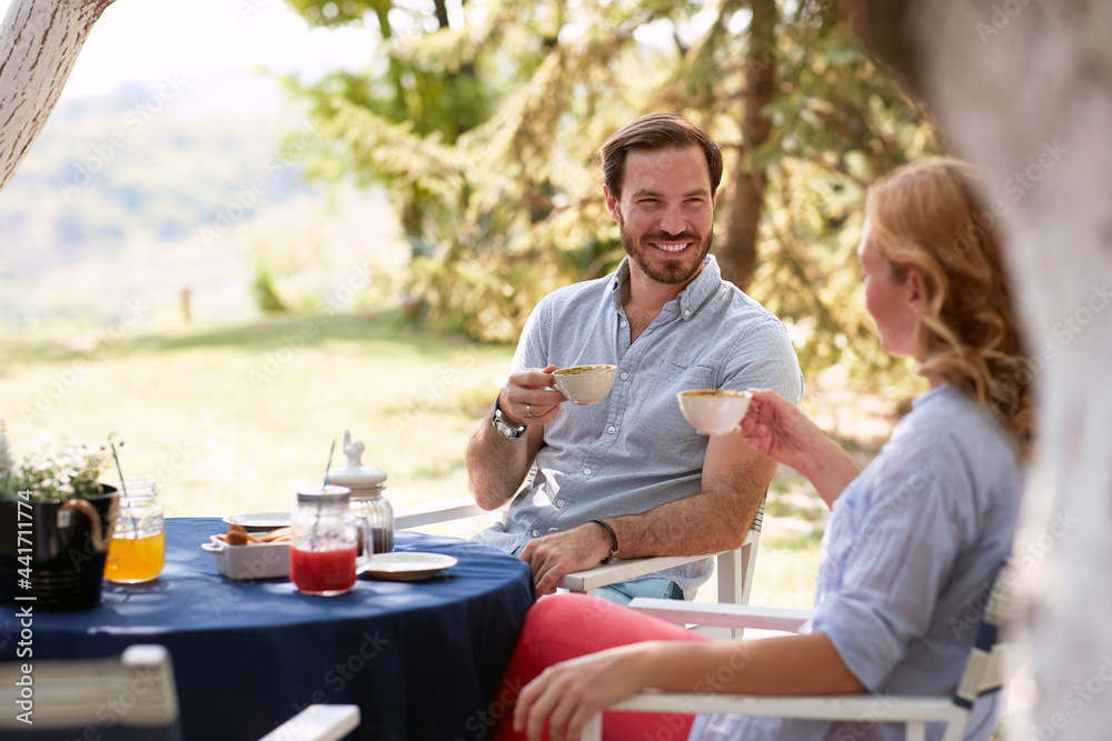 beautiful young adult couple drinking coffee outdoor, sitting at table, smiling, looking each other