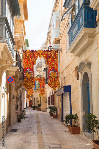 Old narrow street, perspective view with colorful flags decoration, Valletta