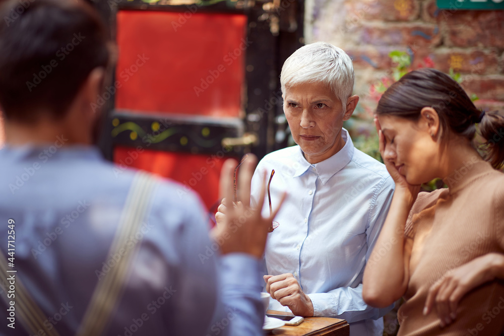 angry mother in law looking reproachfully her son-in-law who is justifying. her daughter sitting beside with her hand on a face, worried. angry mother in law looking reproachfully her son-in-law who is justifying. her daughter sitting beside with her hand on a face, worried.