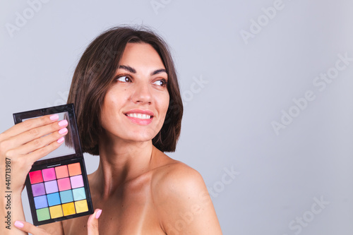 Portrait of natural beauty woman hold bright spring summer colors palette of eye shadows on gray background