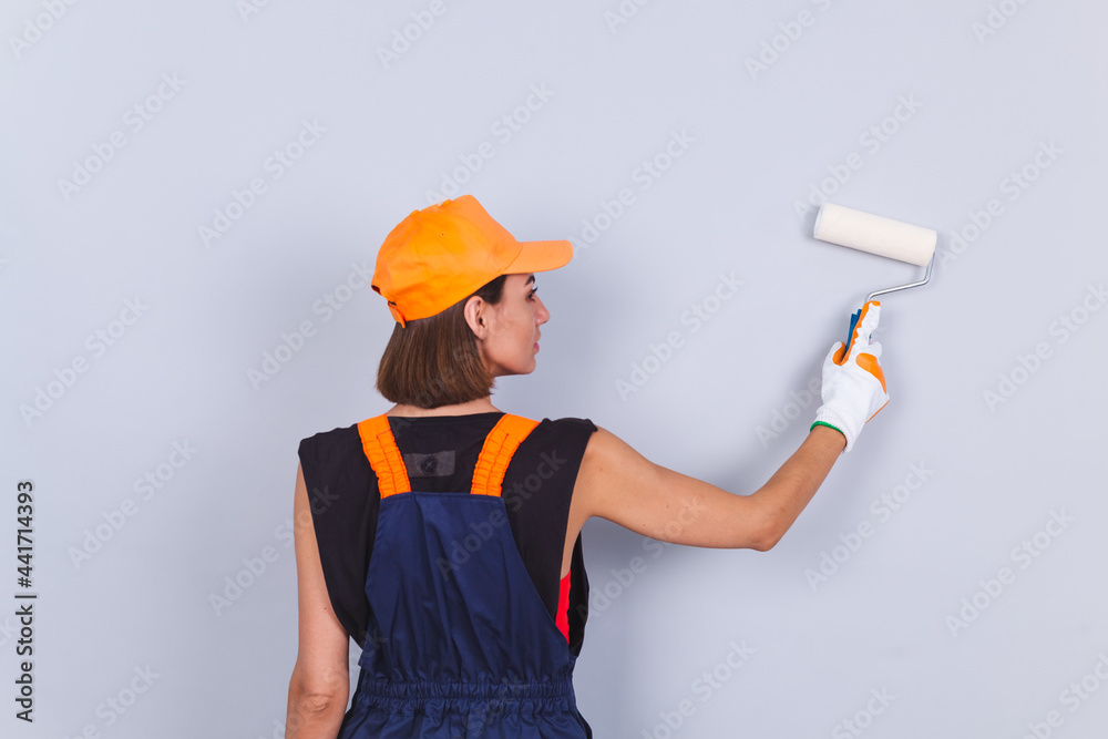 Painter woman with roller brush on gray background positive back to camera paint on wall empty space on right side