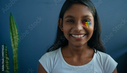 Closeup of a happy dark-skinned girl of the LGBT community smiling vivaciously, wearing pride eye makeup | young teen girl smiling in front of a solid background, representing the happy LGBT community
