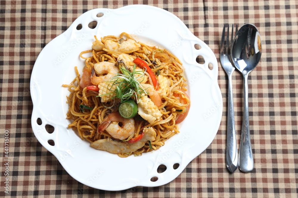 stir fried spicy chilli noodle mamak mee goreng with mixed seafood fish, prawn, squid, meat and lime asian halal menu