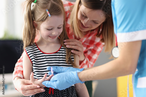 Pediatrician doctor takes blood test from little girl closeup photo