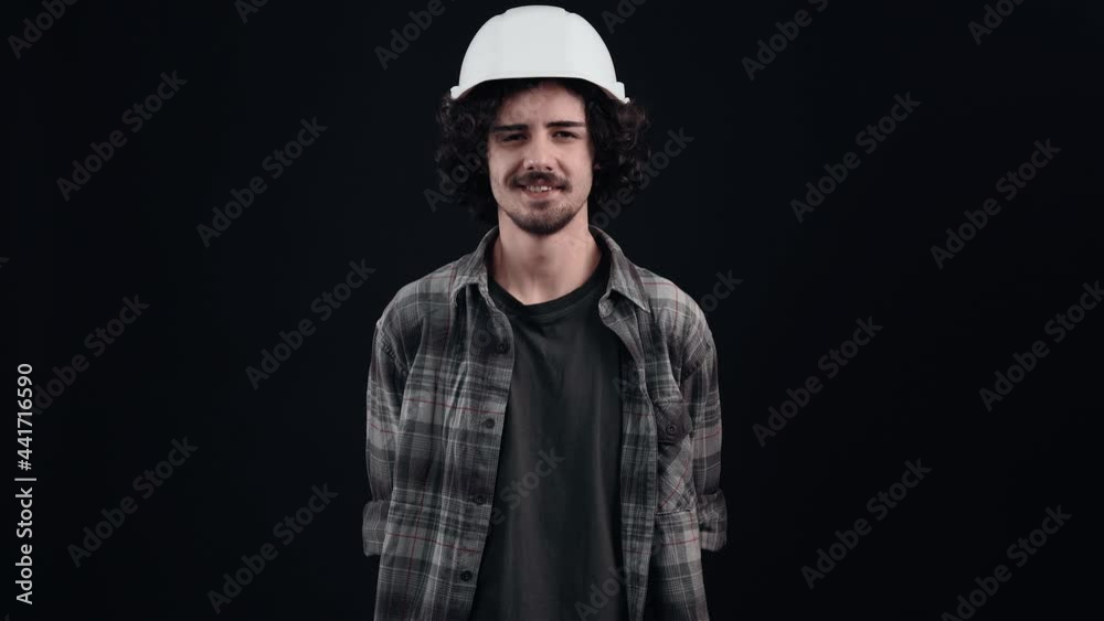 The portrait of the engineer with the white helmet looking at the camera and displaying a wide smile, gives chic eyebrows. Isolated on black background. The concept of life. People's emotions. 4k The portrait of the engineer with the white helmet looking at the camera and displaying a wide smile, gives chic eyebrows. Isolated on black background. The concept of life. People's emotions. 4k