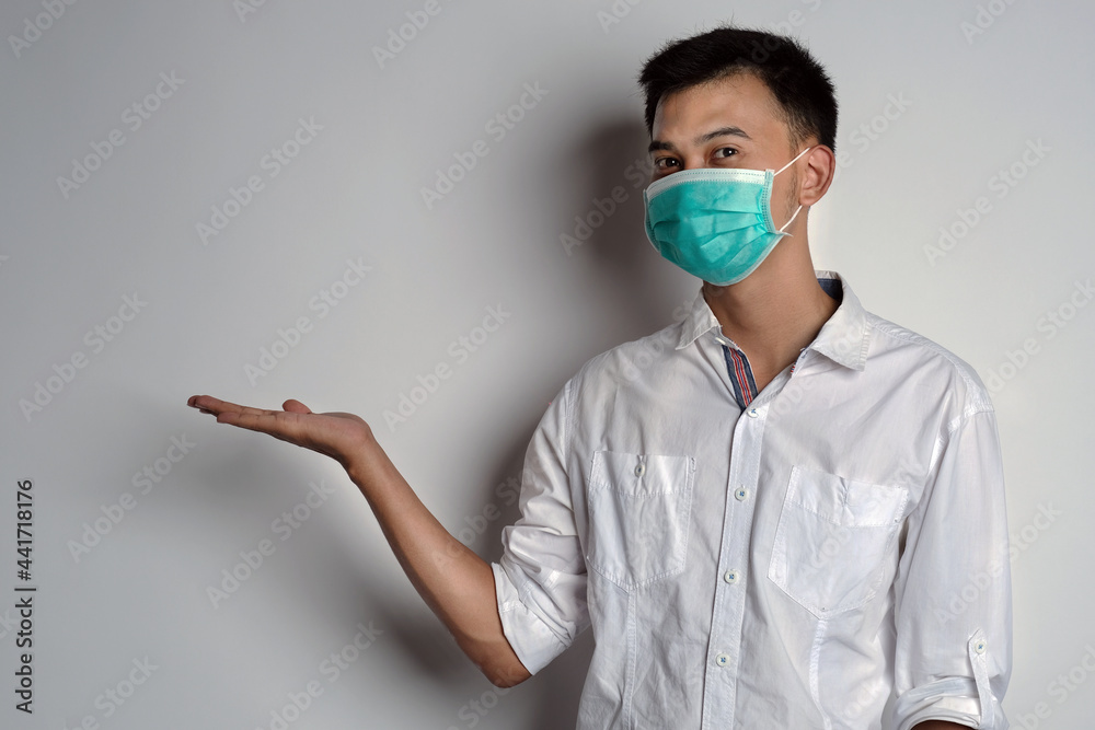 Attractive young asian man wearing a health mask with right hand open gesture against white background. Prevention of the spread of corona virus photography concept. Novel Coronavirus (COVID-19) Attractive young asian man wearing a health mask with right hand open gesture against white background. Prevention of the spread of corona virus photography concept. Novel Coronavirus (COVID-19)