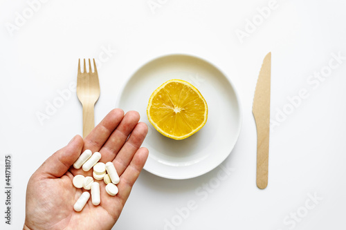 Weibliche Hand mit Tabletten und eine halbierte Zitrone auf einem Telller. Weißer isolierter Hintergrund, Medikament, Draufsicht. photo