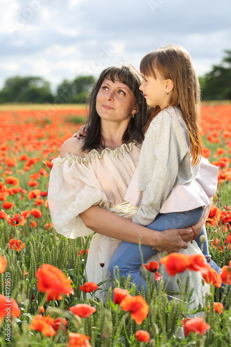 Mom and daughter walk in the poppy field in the evening