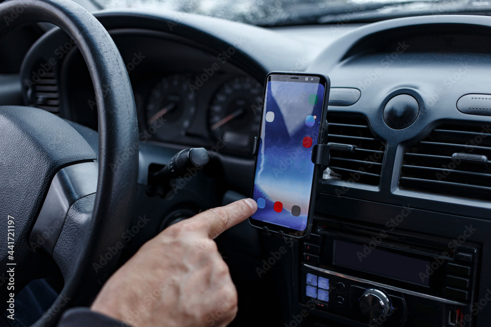 The driver in the car uses a smartphone mounted in a car holder on a torpedo close-up. blurred focus
