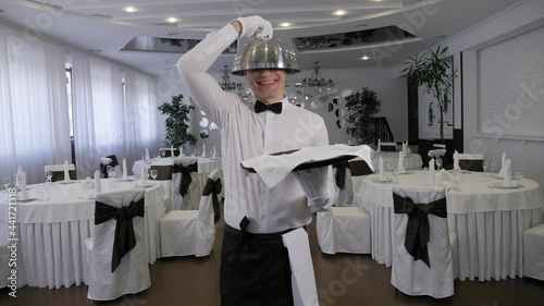 A cheerful waiter is having fun in a restaurant, he puts a metal lid on his head
