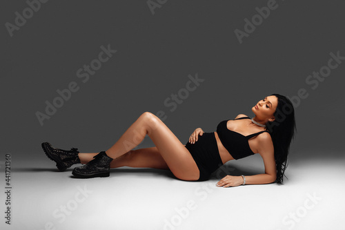 A beautiful pregnant girl in a black image lies on the white floor. Fashionable dark style. Beautiful pregnancy time