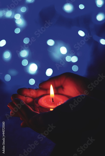 Burning candle in the hands of a girl with bokeh light. Christmas candles. Candlelight glowing in woman's hands. Praying, faith, religion concept.