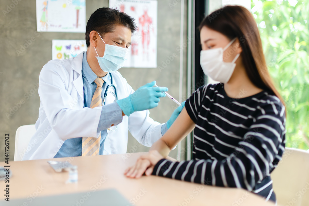Obraz premium Senior doctor syringe injection vaccine to the young patient put on a mask in the hospital.Medical healthcare concept.