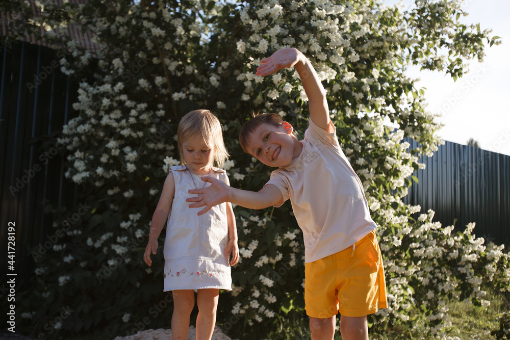 Fototapeta premium a boy in yellow shorts waves his hands and smiles, and his younger sister is standing next to him