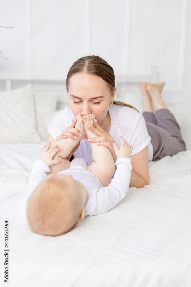 mother kisses baby's feet and sniffs them on the bed at home, happy motherhood mother kisses baby's feet and sniffs them on the bed at home, happy motherhood
