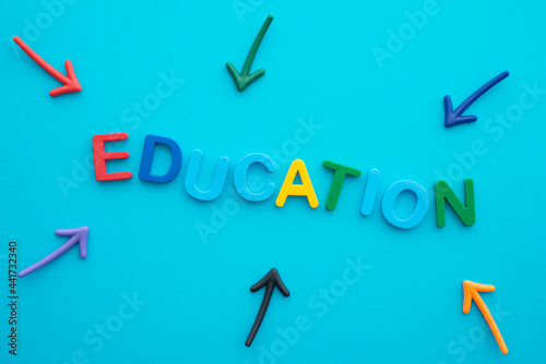 Flat lay of colorful letters alphabet EDUCATION on blue background with arrow around. Educational and back to school concept.