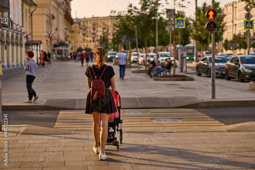 young woman in black clothes walks around the city with a stroller. A beautiful and thin mother on a walk with a newborn baby and a yoya stroller on the streets of a metropolis on a sunny summer day.