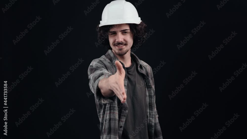 The novice, benevolent engineer, with a white helmet, extends his friendly hand to greet. Isolated on black background. The concept of life. People's emotions. 4k portrait The novice, benevolent engineer, with a white helmet, extends his friendly hand to greet. Isolated on black background. The concept of life. People's emotions. 4k portrait